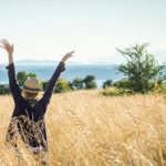 woman's back in tall grass field with arms up