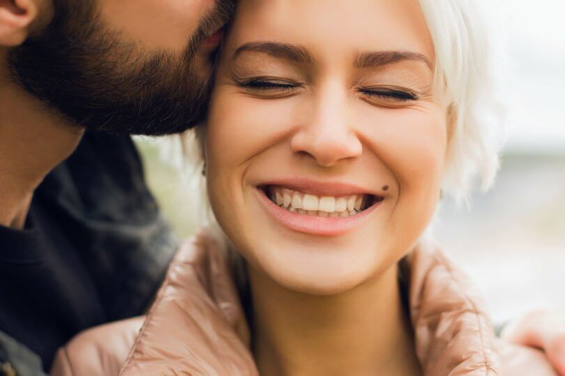 woman smiling while being kissed on the forehead by a man